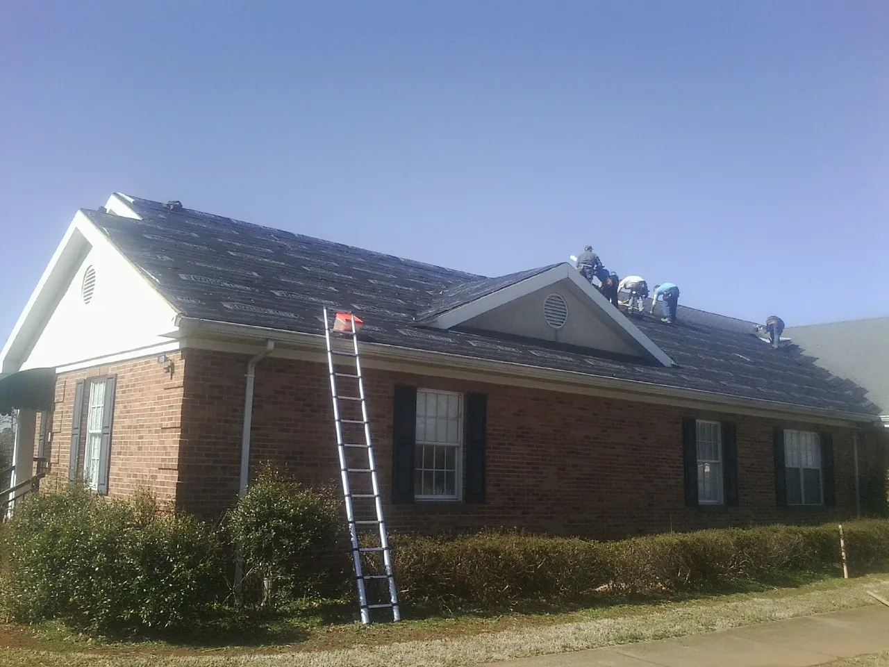 Crew tearing shingles off a brick ranch roof with a ladder set — Metal Roof Repair work by our crew in Camano Island
