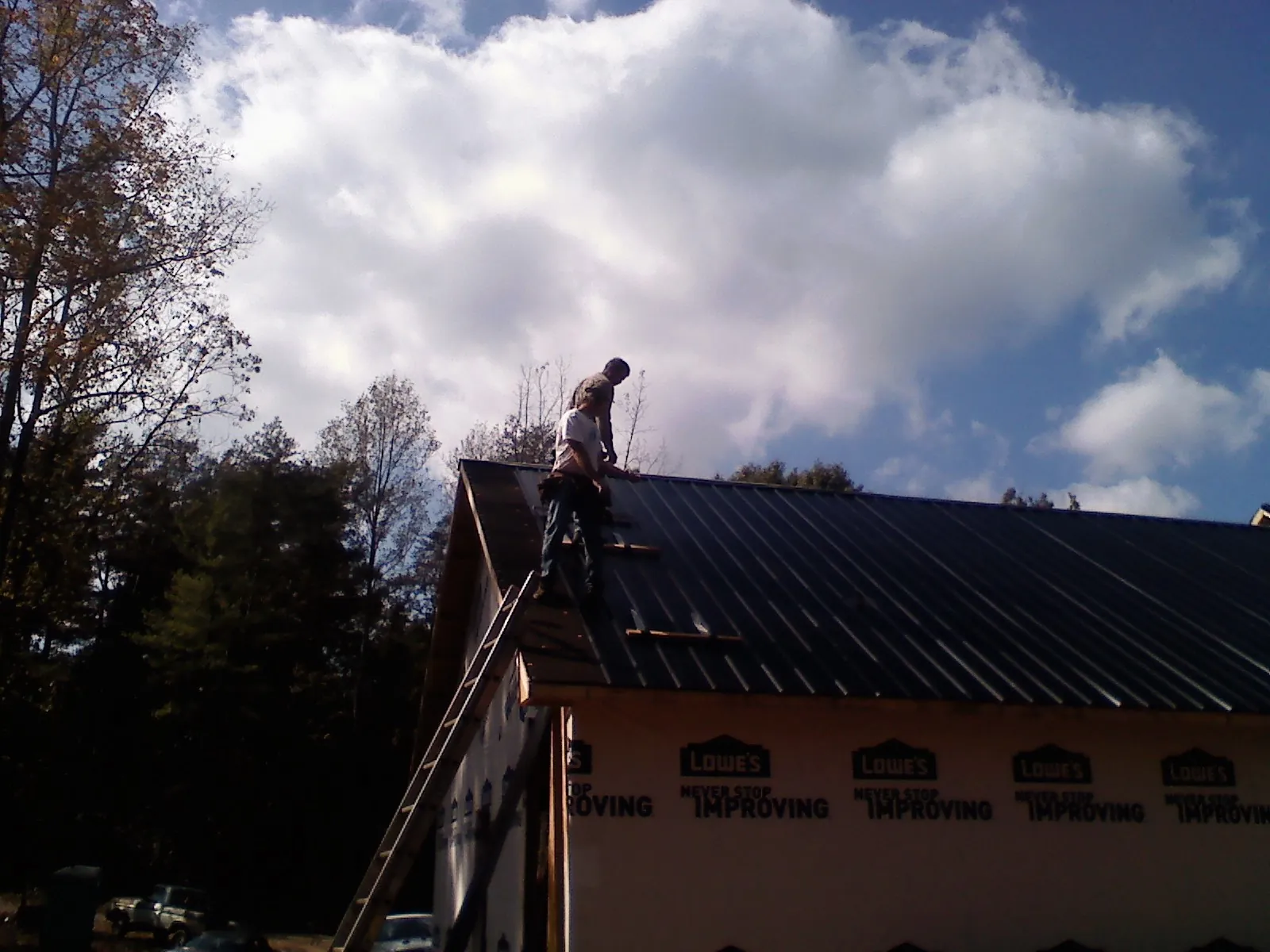 Roofer fastening dark metal panels high against a cloudy sky, from a Roof Inspection job in Camano Island