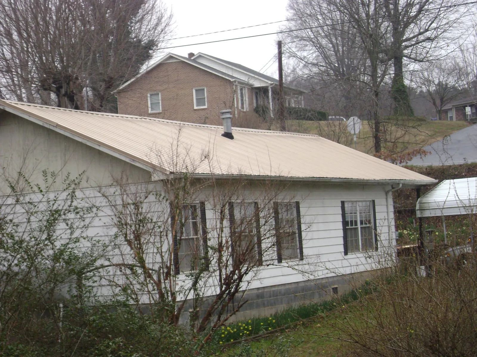 Tan metal roof on a white sided house set into a hillside — Commercial Roofing by Roofing Brothers in Camano Island